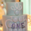 Whimsical four tiered mint green cake with white fondant accents and glitter text