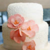 While three tier cake with champagne ribbon trim, peach floral accents and coordinated cupcakes