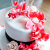 White three tier cake with black fondant ribbon trim, red and cream floral accents and monogram crystal topper