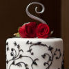 White two tier cake with silver metal base, black vine accents and red rose topper