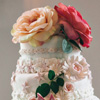 Four tier cake with white and pink floral icing accents and large peach and coral flower topper