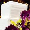 White three tier cake with textured base, white fondant ribbon trim and yellow and purple floral accents