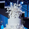 Five tier white cake with embossed metallic base and floral and feather accents and topper