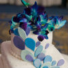 Modern three tier white cake with pearl beads, purple, blue and teal fondant accents and blue gradient snap dragon flowers. 
